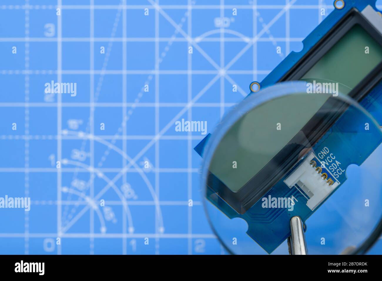 Primo piano della scheda a circuito stampato con display lcd tenuto da clip a coccodrillo visibili attraverso la lente di ingrandimento su sfondo blu. Foto Stock