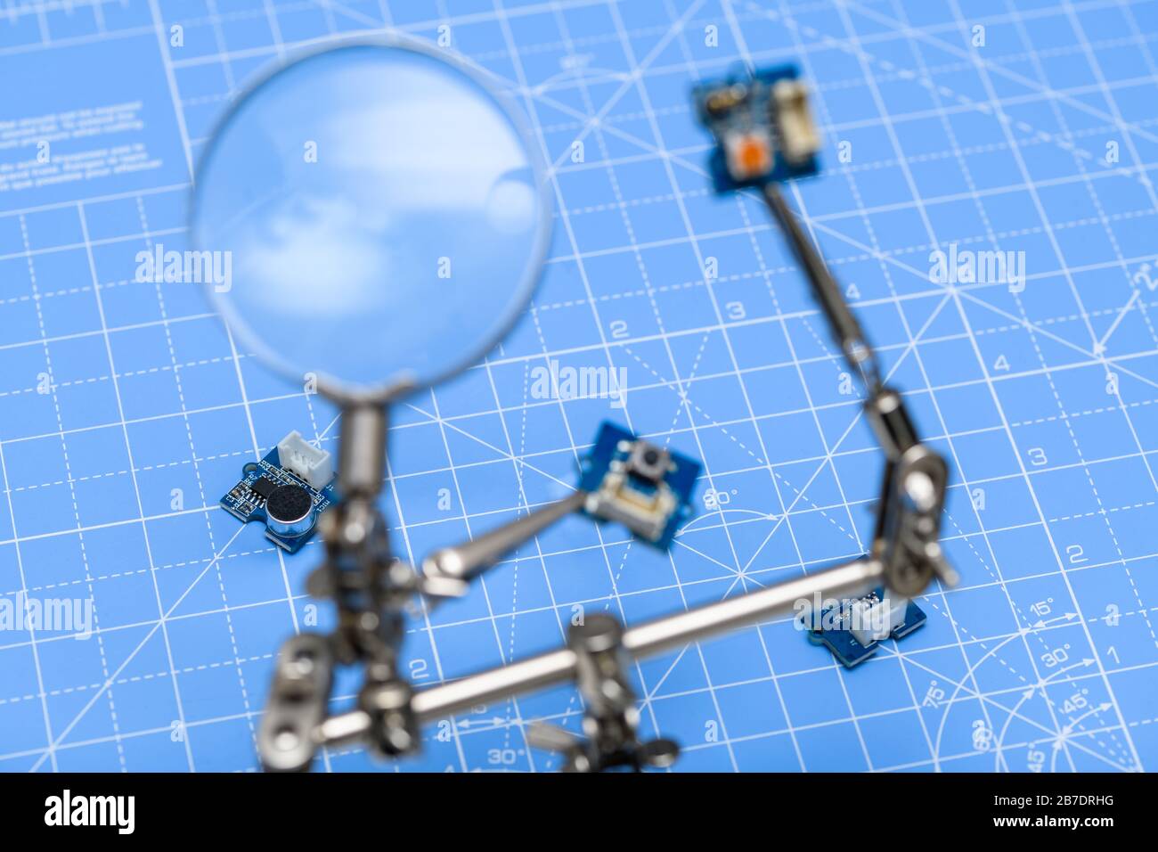 Circuiti stampati su sfondo blu con pannelli sfocati tenuti da clip a coccodrillo e con lente di ingrandimento in primo piano. Foto Stock