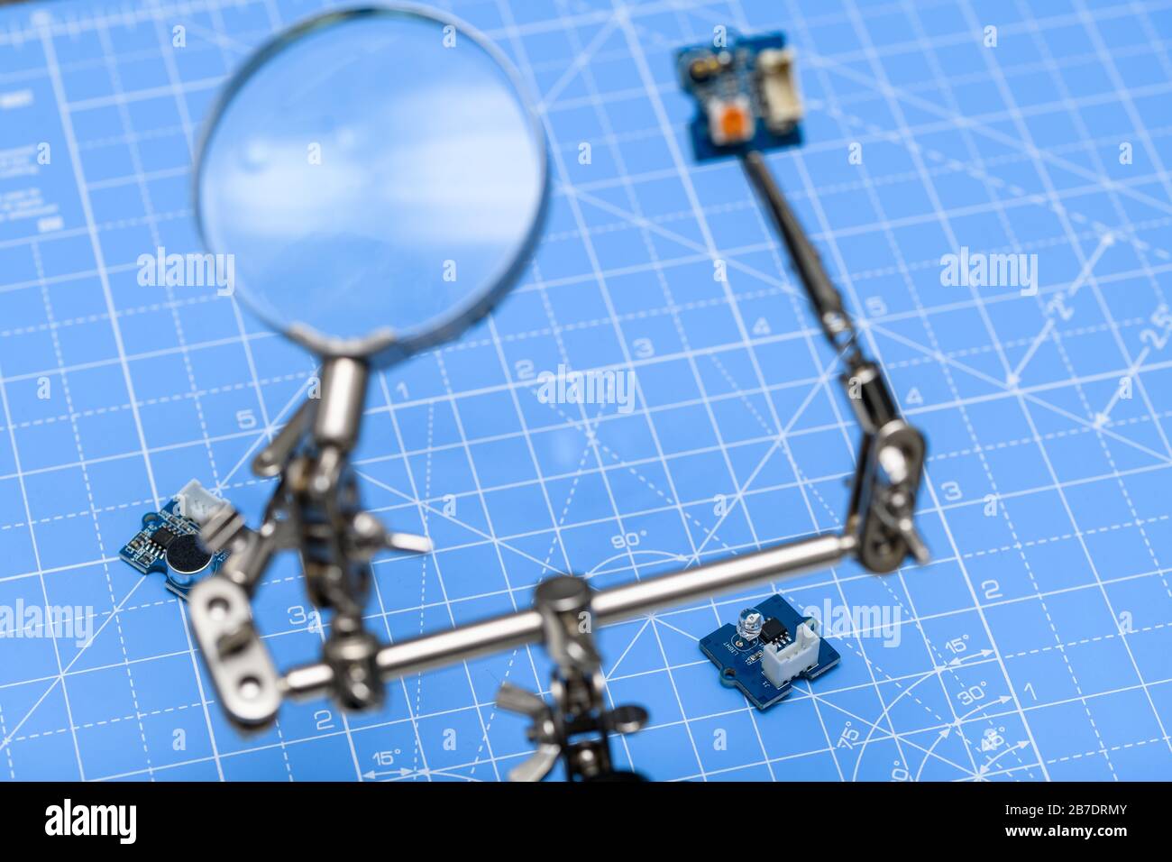 Circuiti stampati su sfondo blu con pannello sfocato tenuto da clip a coccodrillo e con lente di ingrandimento in primo piano. Foto Stock