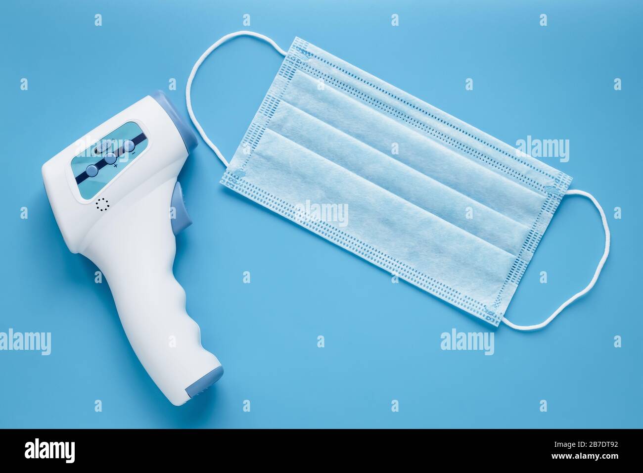 Maschera medica e termometro elettronico senza contatto per la misurazione della temperatura, sfondo blu Foto Stock
