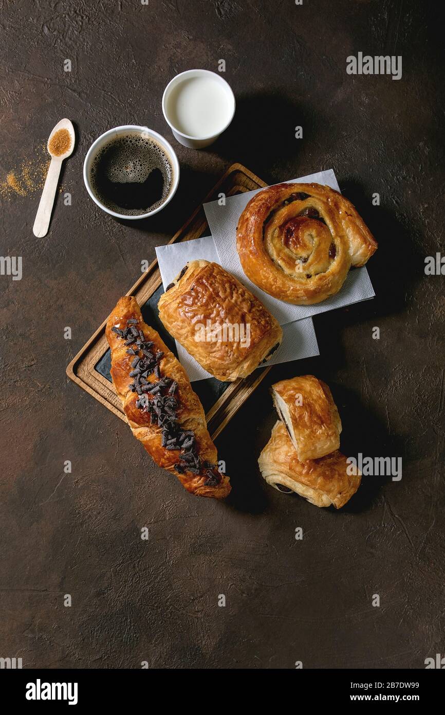 Varietà di panini tradizionali francesi con rasin e cioccolato, croissant con tazza di carta di caffè e latte, cucchiaio di legno riciclato di su di canna Foto Stock