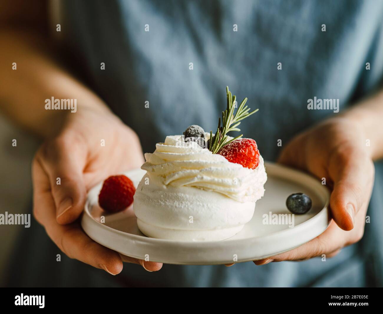 Piatto da donna con mini Pavlova torta decorata con frutti di bosco freschi e rosmarino Foto Stock