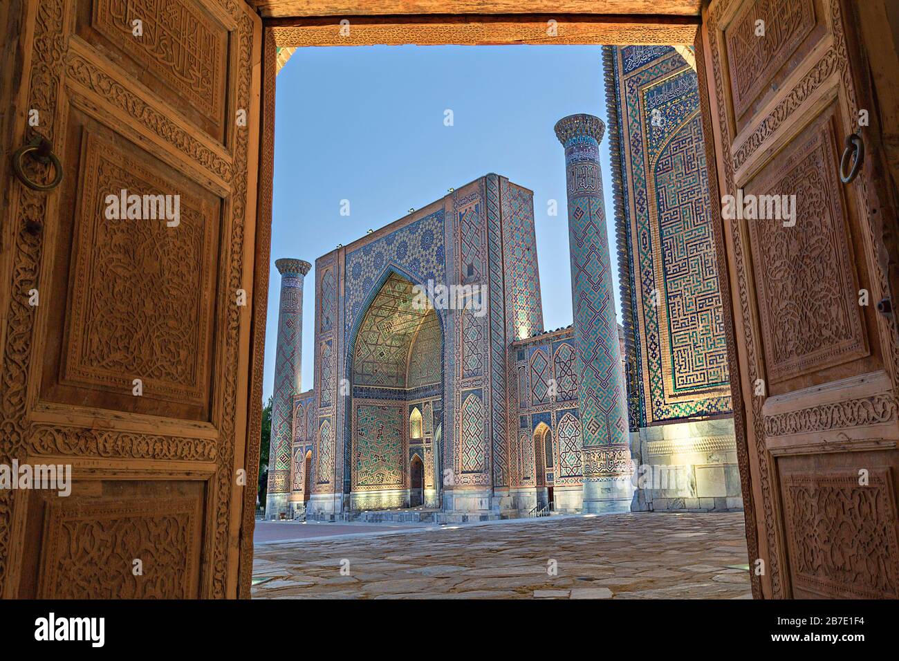 Vista sulla madrassa in Piazza Registan, attraverso porte in legno, a Samarcanda, Uzbekistan. Foto Stock