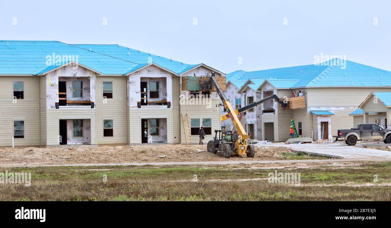 Ricostruzione di Salt Grass Landing Apartments. Operatori che installano il rivestimento del finestrino, rialzato con il sollevatore per materiali Caterpillar. Foto Stock