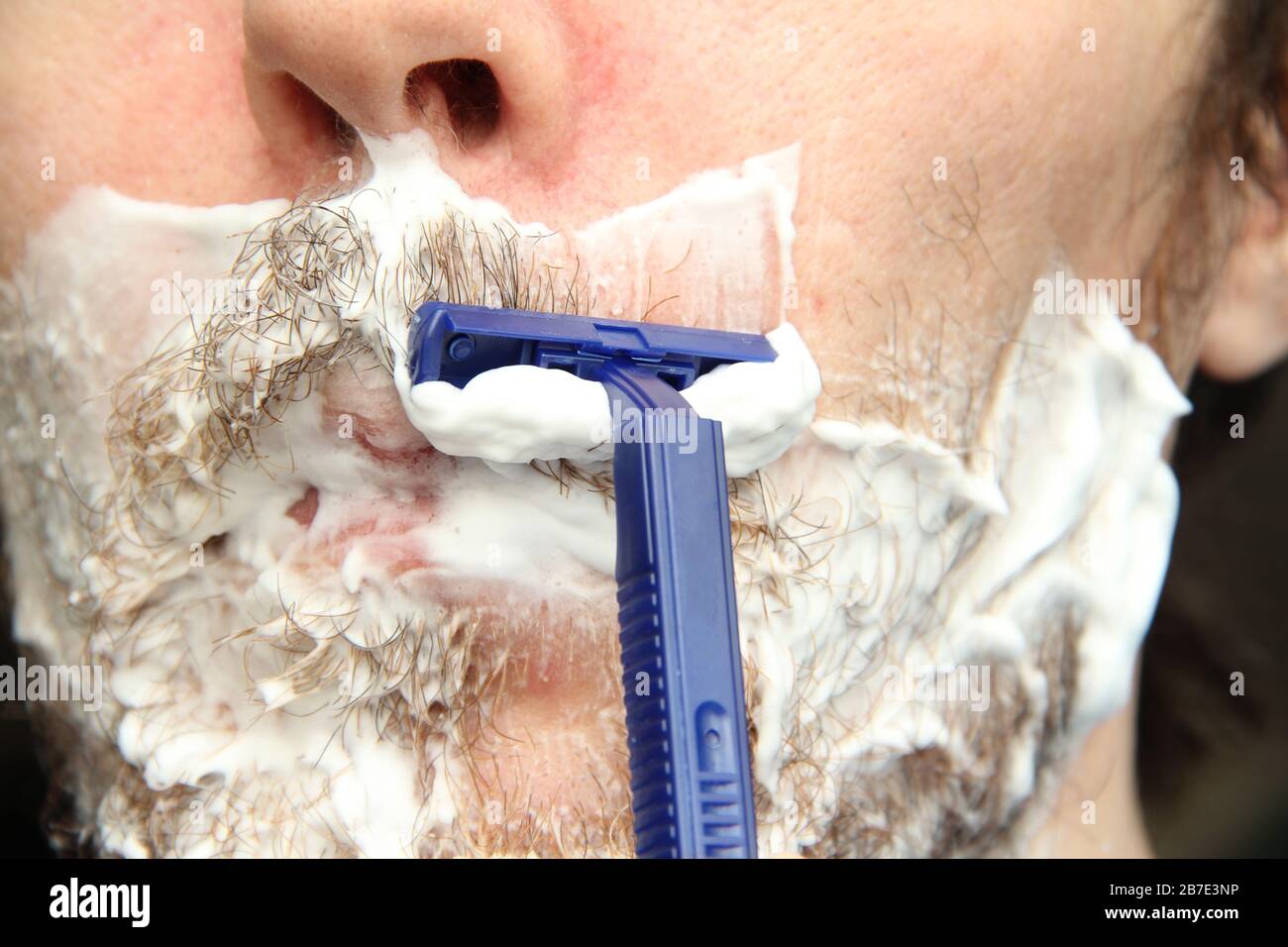 Un uomo rasa la barba con un rasoio di sicurezza monouso blu. Schiuma da  barba bianca sulle guance e sul mento Foto stock - Alamy