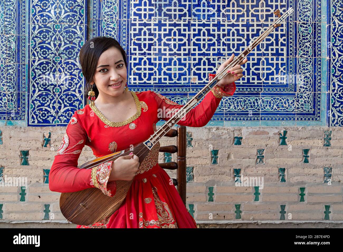 Donna uzbeka in costume nazionale che gioca strumento musicale locale del Dutar, a Khiva, Uzbekistan Foto Stock
