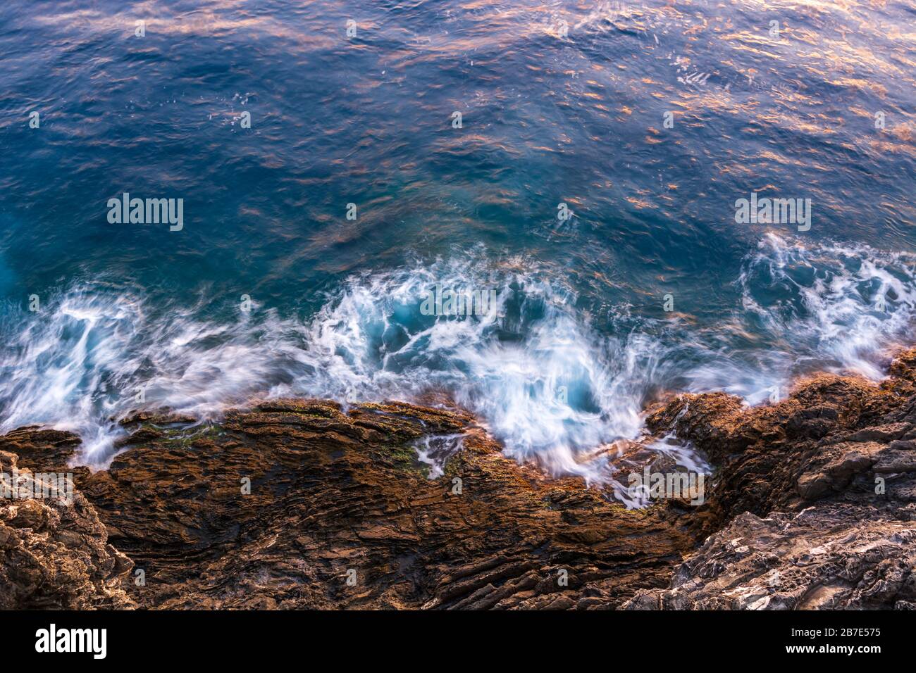 Onde che si schiacciano sulle scogliere come visto dall'alto durante il tramonto Foto Stock