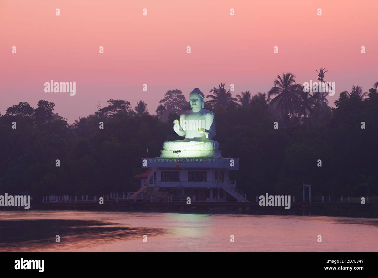 BENTOTA, SRI LANKA - 16 FEBBRAIO 2020: Una vista di una scultura di un Buddha seduto in mezzo a un'alba rosa. Bentota Udakotuwa Tempio Foto Stock