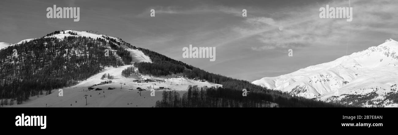 Panorama bianco e nero di piste da sci innevate con skilift, tracce e foreste in alta montagna d'inverno e cielo nuvoloso illuminato dalla luna al mattino. Itali Foto Stock