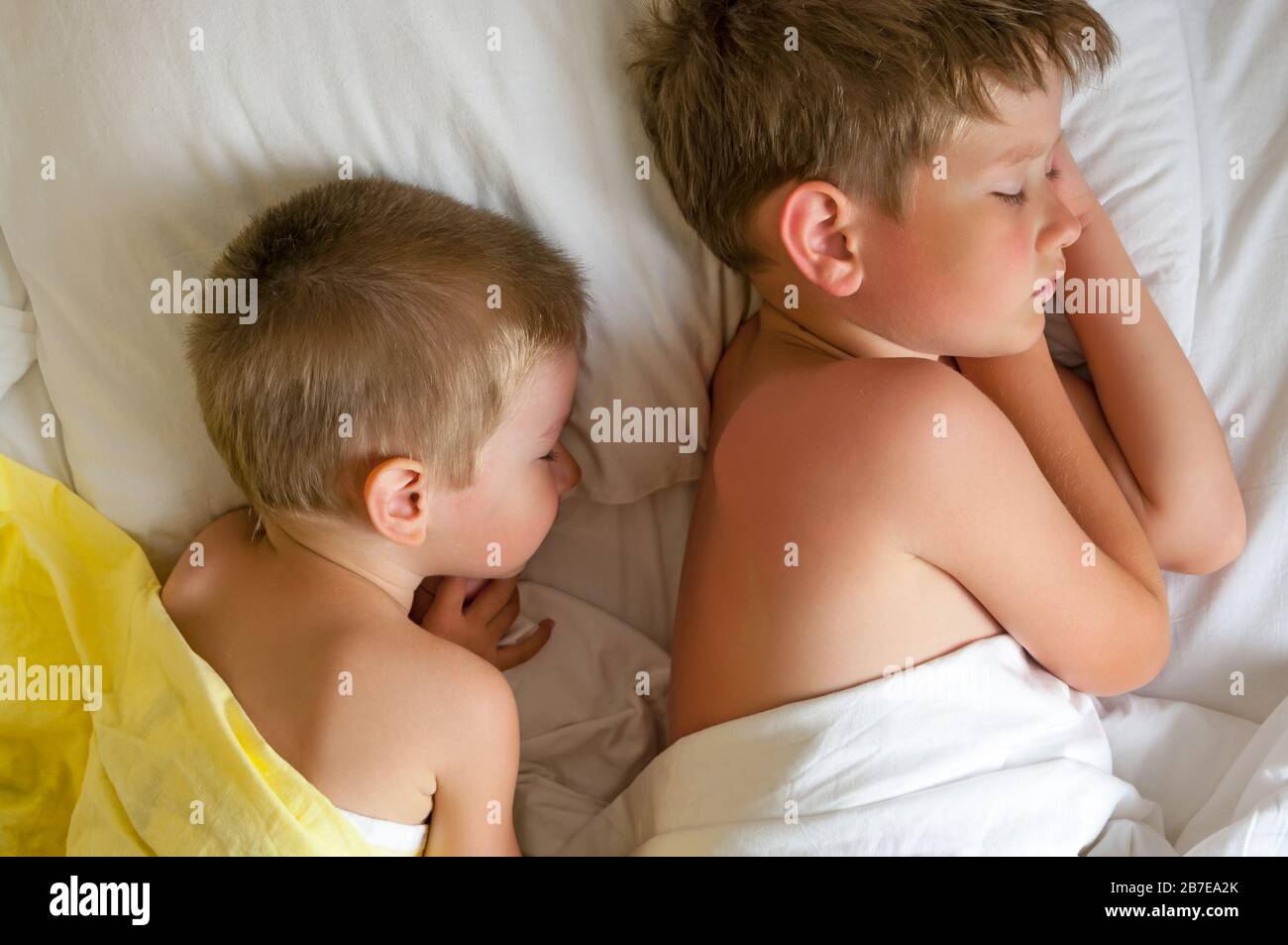 Due fratelli dormienti su un letto con copriletto bianco. Foto Stock