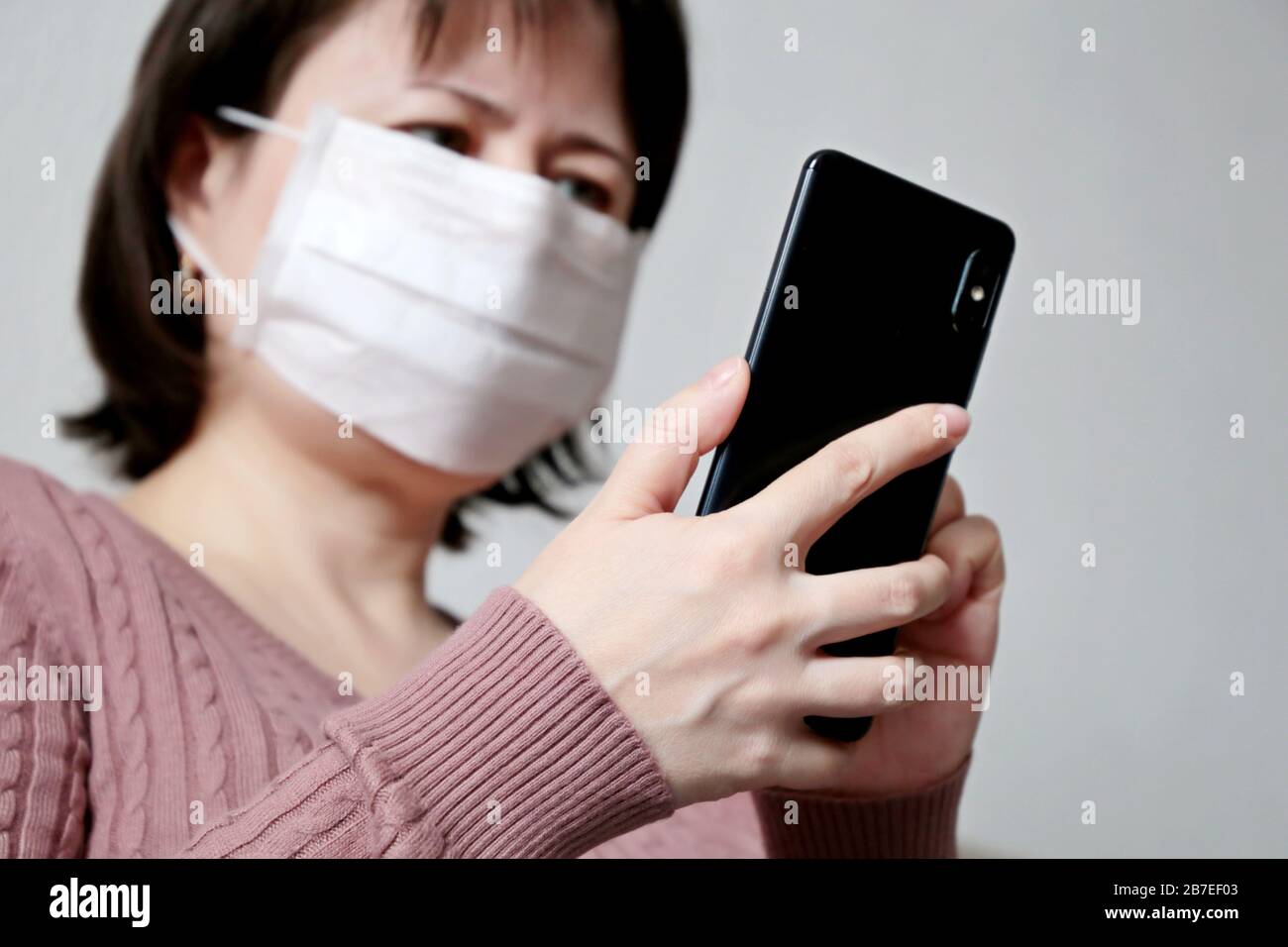 Donna in maschera medica con smartphone, telefono cellulare in primo piano in mani femminili. Concetto di malattia, febbre, raffreddore e influenza, ricerca del sintomo di coronavirus Foto Stock