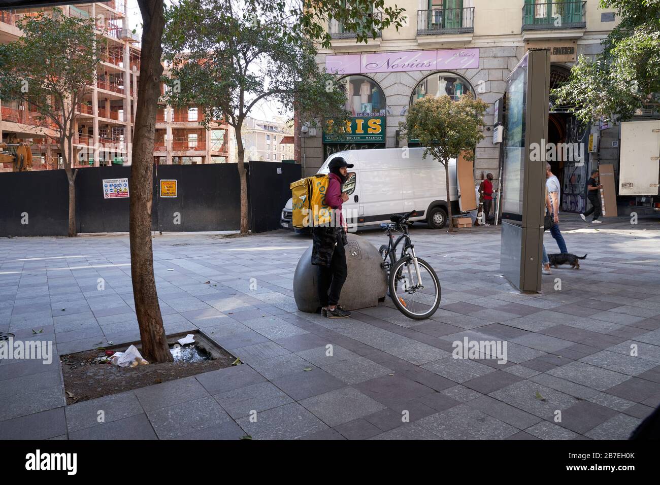 Un ciclista di consegna del globo attende fuori di un deposito nel centro di Madrid, è principalmente camminatori del cane e consegnano la gente fuori durante lo stato di emergenza Foto Stock