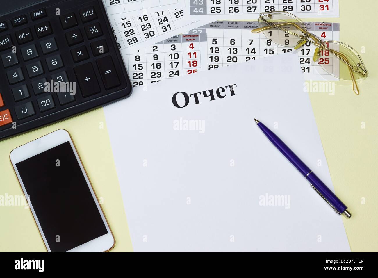 Il titolo del rapporto in lingua russa su una pagina vuota, una calcolatrice, uno smartphone, occhiali da sole e un calendario. Il luogo di lavoro della testa Foto Stock