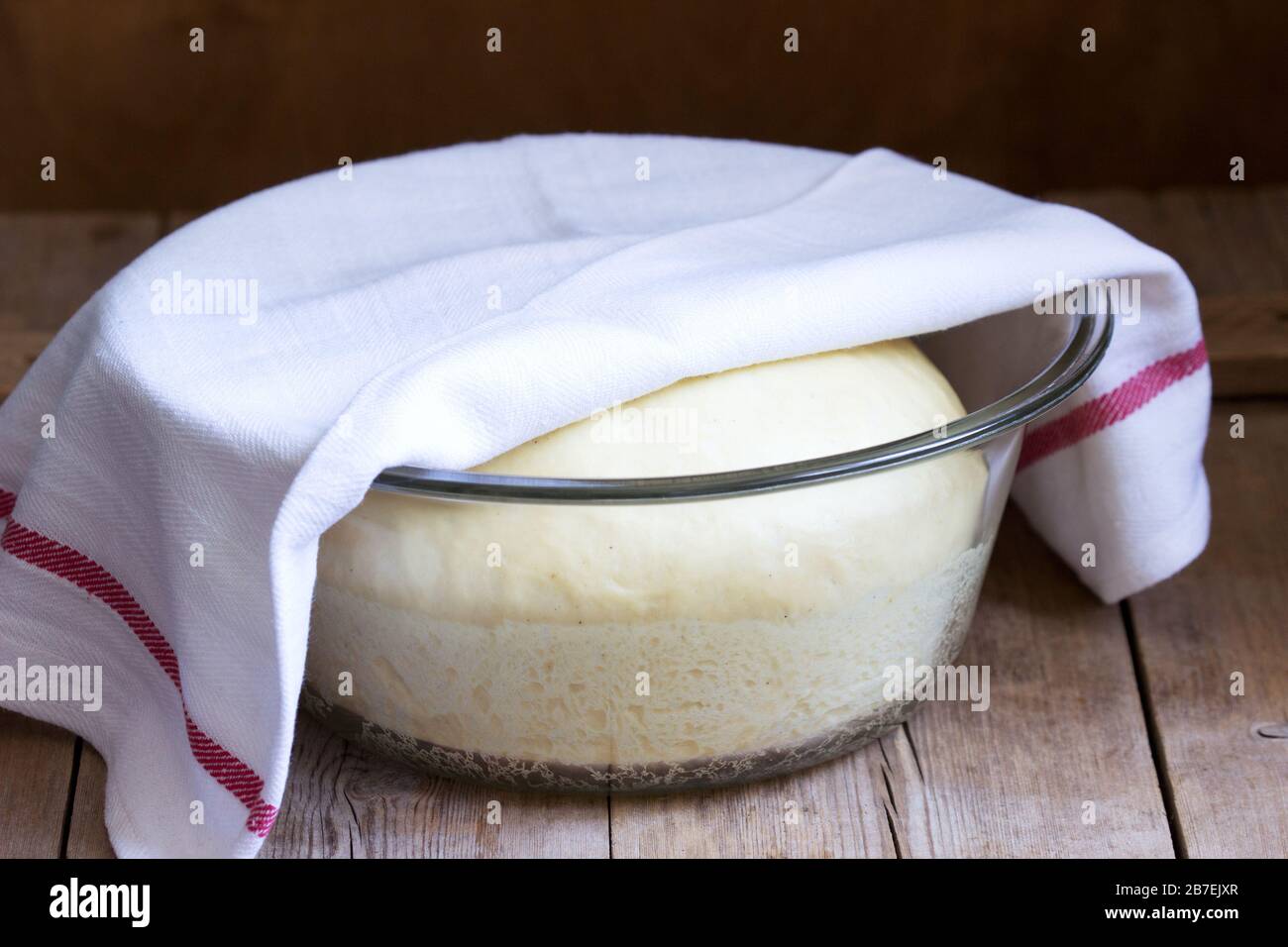 Pasta di lievito in una ciotola di vetro su un tavolo di legno. Stile rustico,. Foto Stock