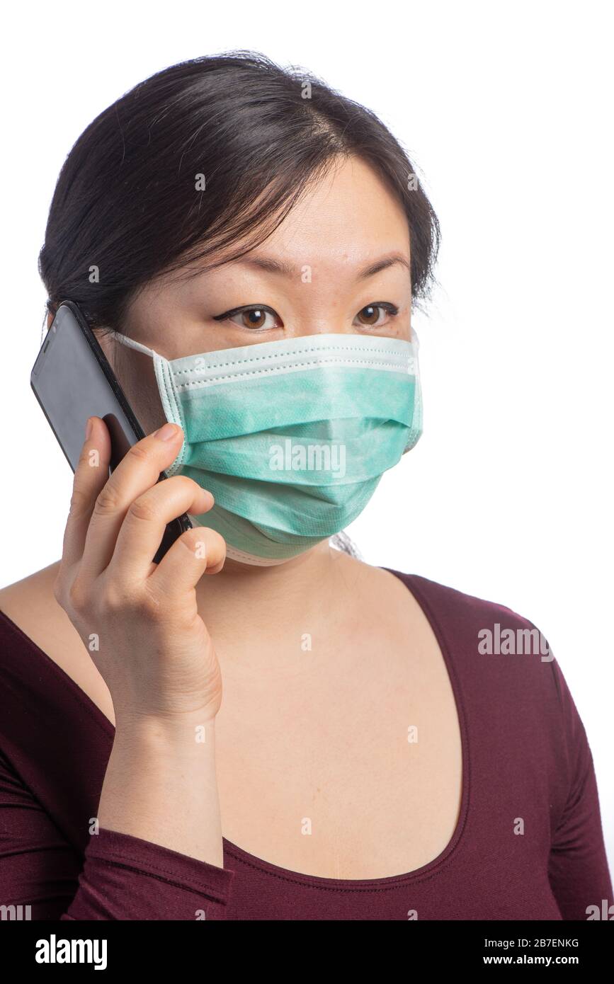 giovane donna asiatica che indossa una maschera di protezione verde facendo una chiamata telefonica su uno sfondo bianco Foto Stock