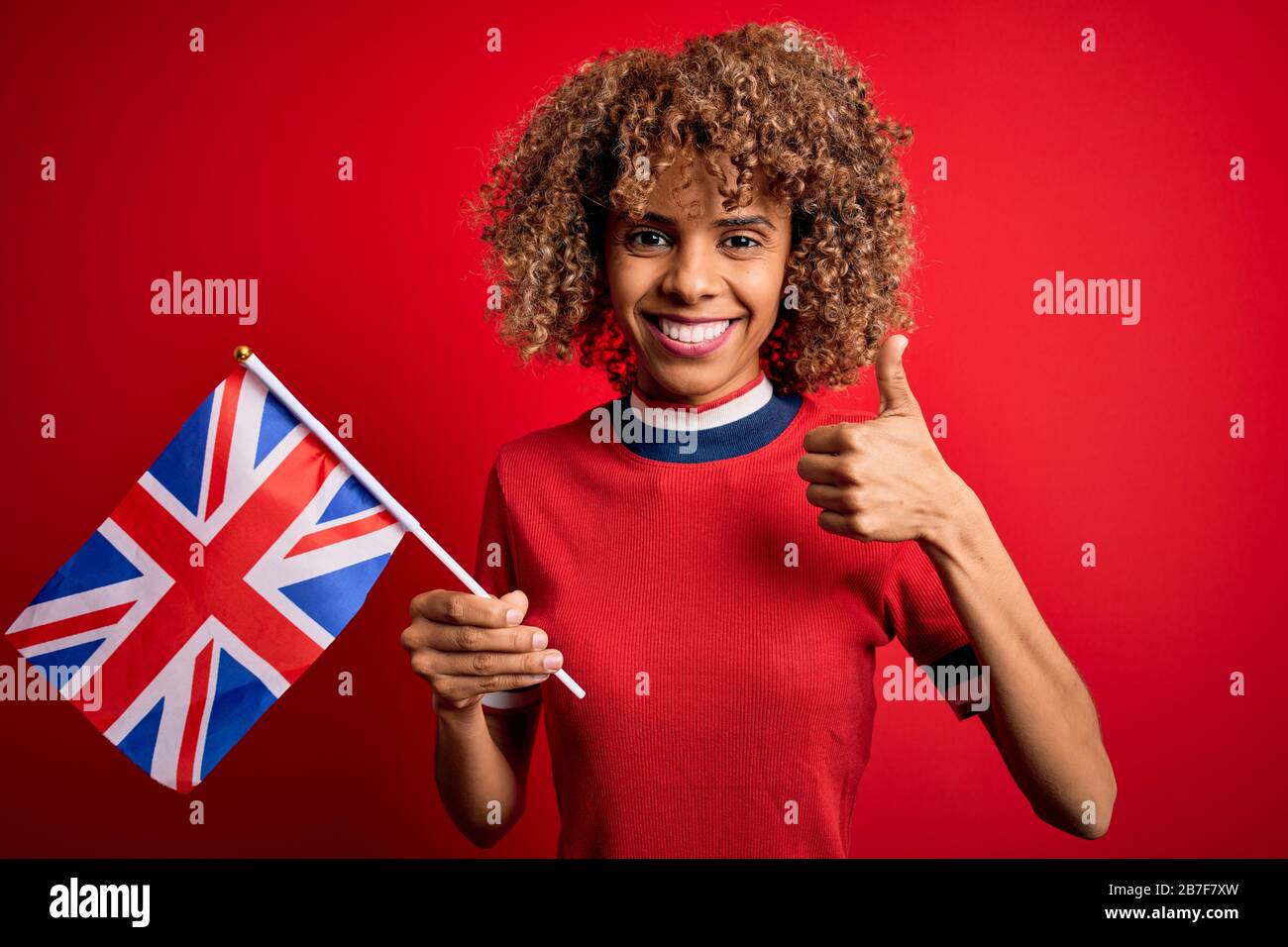 Giovane maledetta afro-americana che tiene la bandiera del regno unito per celebrare il referendum sulla brexit felice con un grande sorriso fare il segno ok, pollice in su con le dita, eccellente Foto Stock