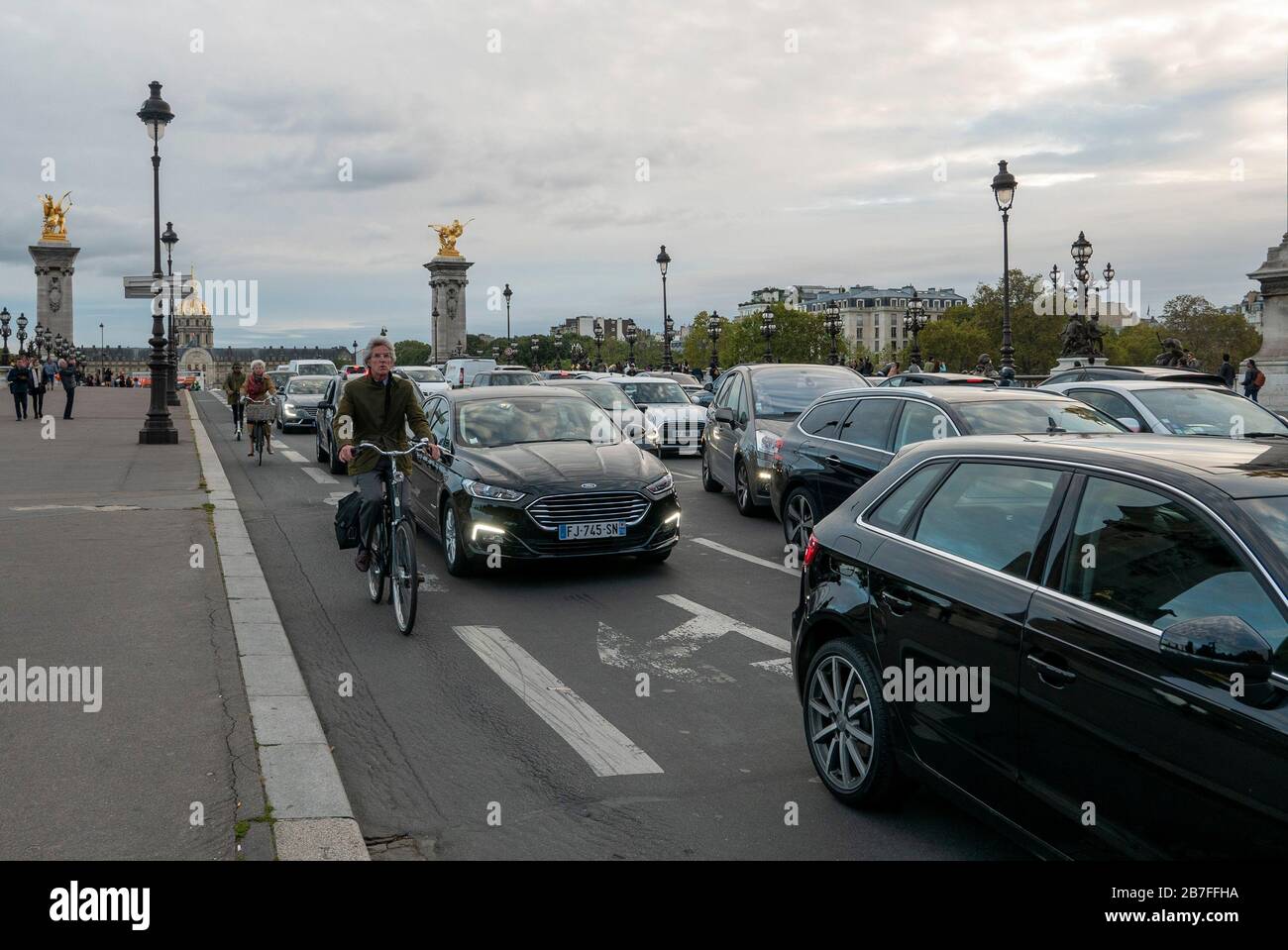 I ciclisti passano accanto a auto in lento movimento in un ingorgo durante l'ora di punta sul Pont Alexandre III a Parigi, Francia, Europa Foto Stock