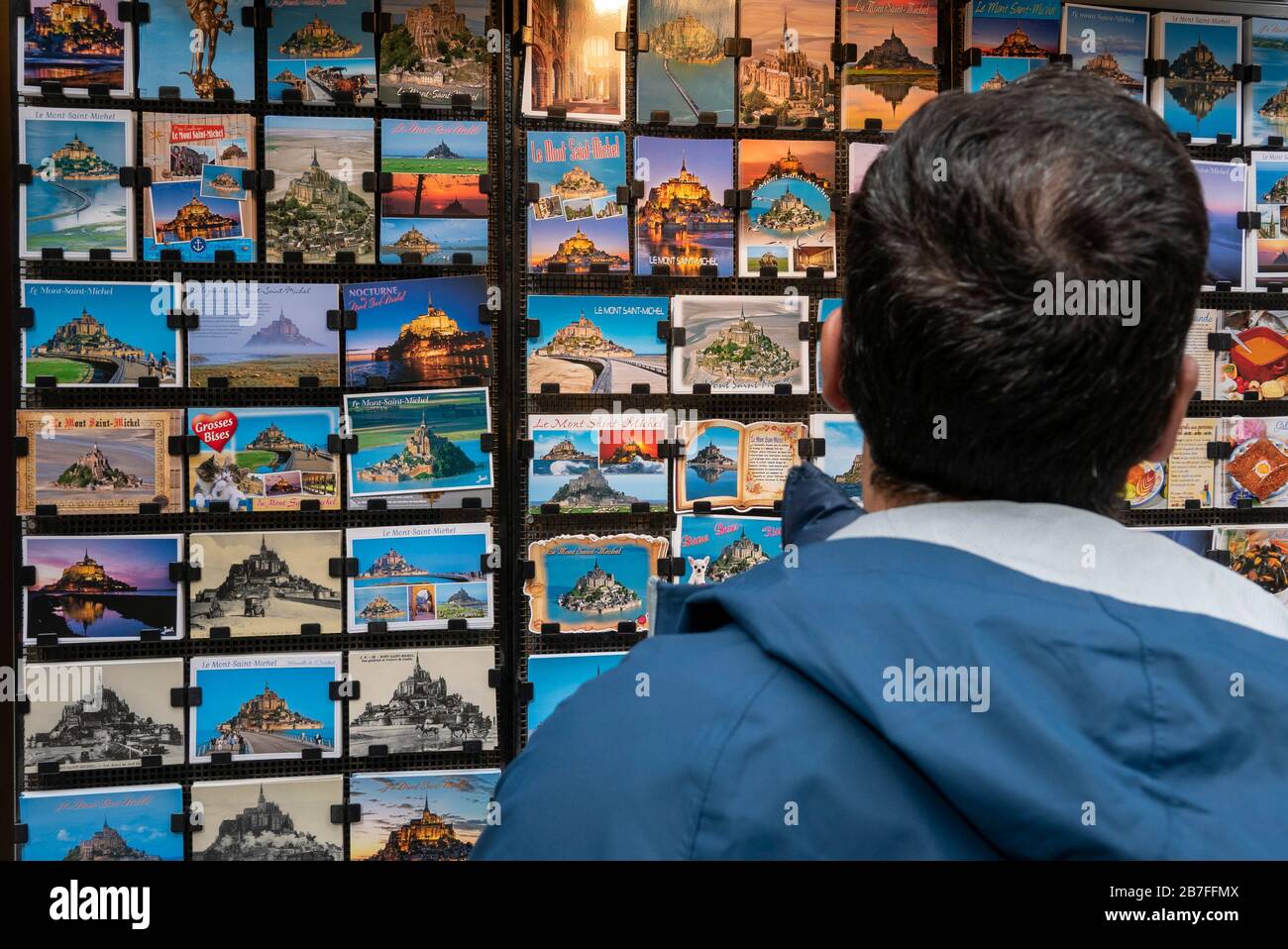 Uomo che guarda le cartoline di Mont Saint-Michel esposte in un negozio di souvenir Foto Stock