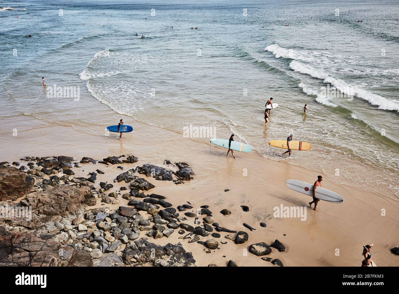 Piccolo gruppo di giovani che si dirigono nell'oceano portando tavole da surf a Little Cove, Noosa, Queensland Foto Stock