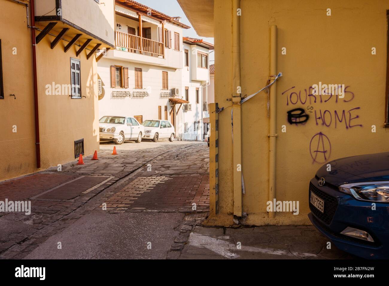 'I turisti vanno a casa' è cambiato in 'turisti B casa' - anti-turismo ha trasformato graffiti pro-turismo su un muro a Salonicco, Grecia Foto Stock