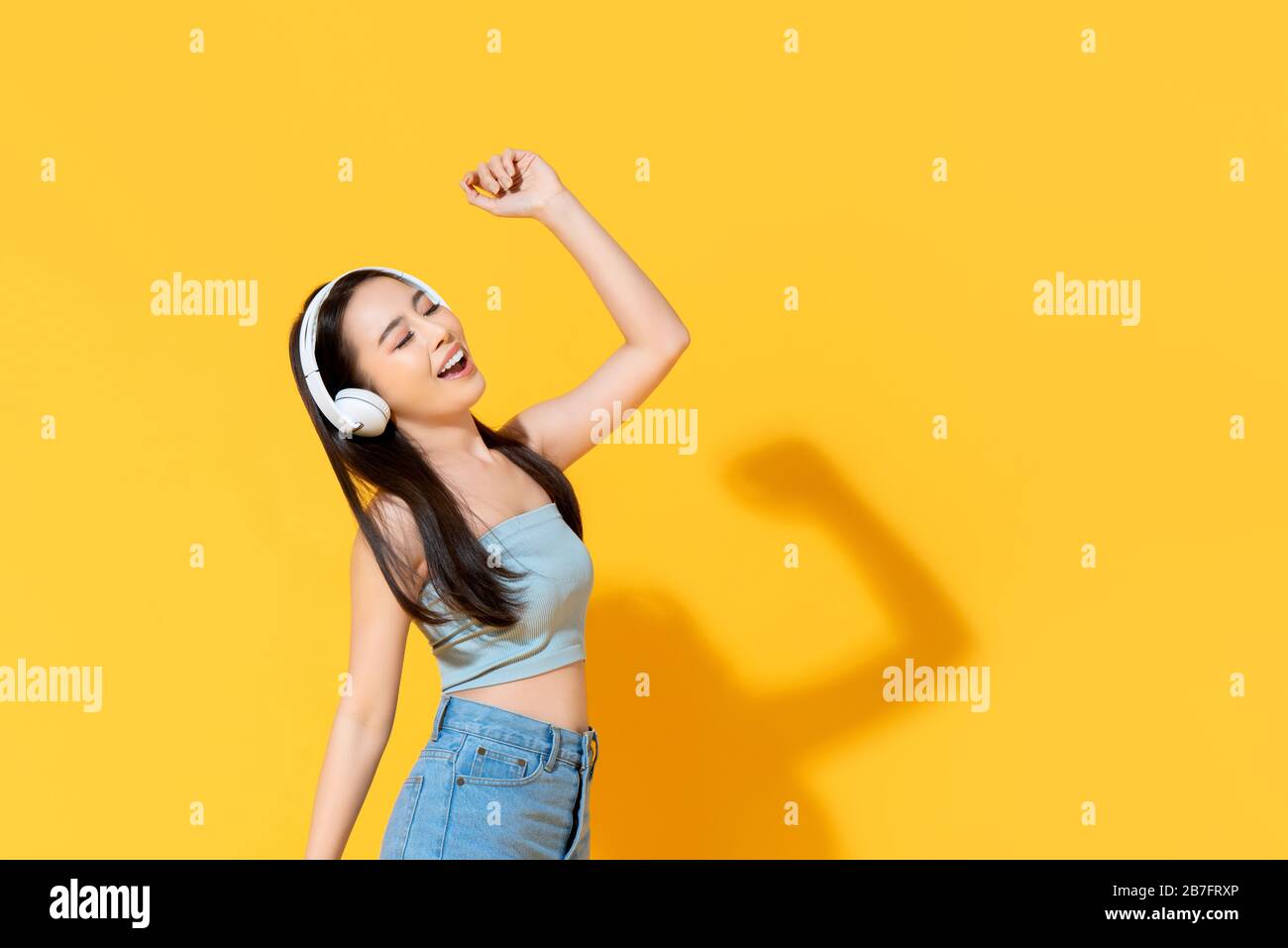 Felice giovane donna asiatica in estate indossare ascoltare musica da cuffie e danza isolato su sfondo giallo Foto Stock