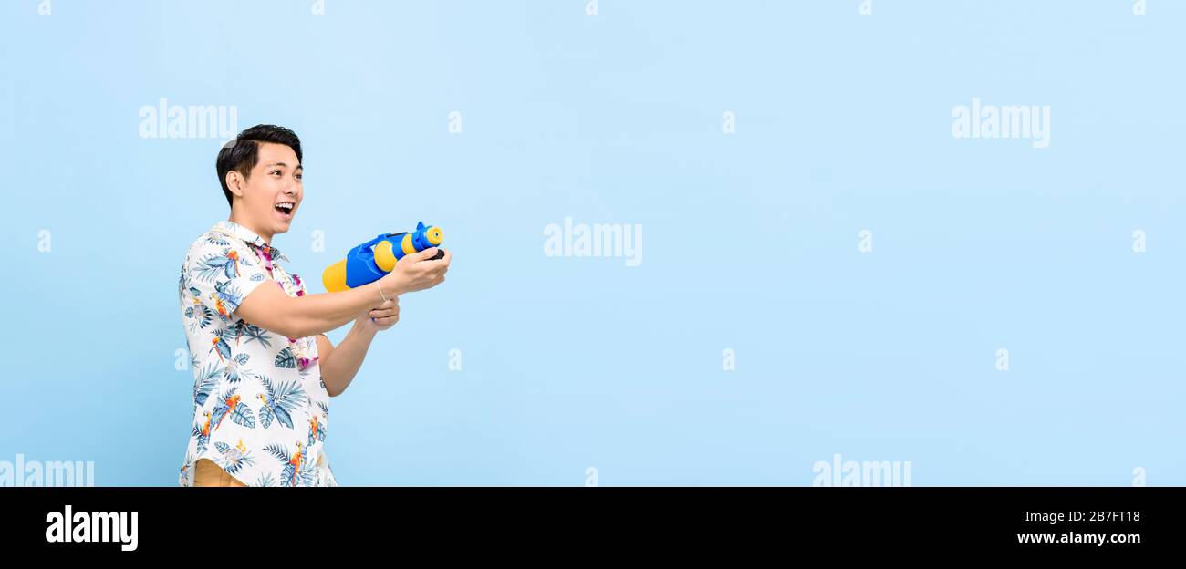 Sorridente bell'uomo asiatico che gioca con pistola ad acqua isolato su sfondo blu banner con spazio per copia per Songkran festival in Thailandia e sud-est A. Foto Stock