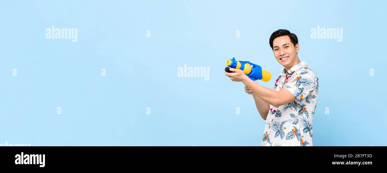 Sorridente bell'uomo asiatico che gioca con pistola ad acqua isolato su sfondo blu banner con spazio per copia per Songkran festival in Thailandia e sud-est A. Foto Stock