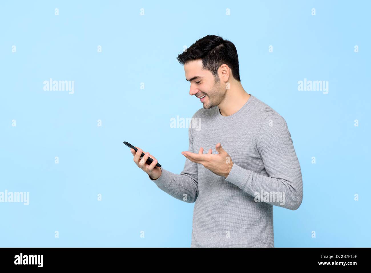 Sorridente giovane felice utilizzando smartphone isolato su sfondo blu chiaro studio Foto Stock