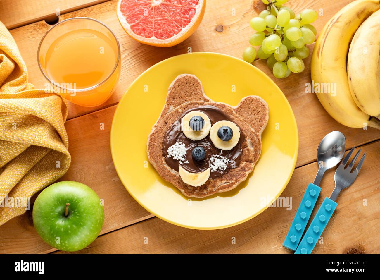 Colazione per bambini con frittelle, frutta e succo di frutta sorridenti. Arte alimentare, genitorialità e concetto di maternità Foto Stock