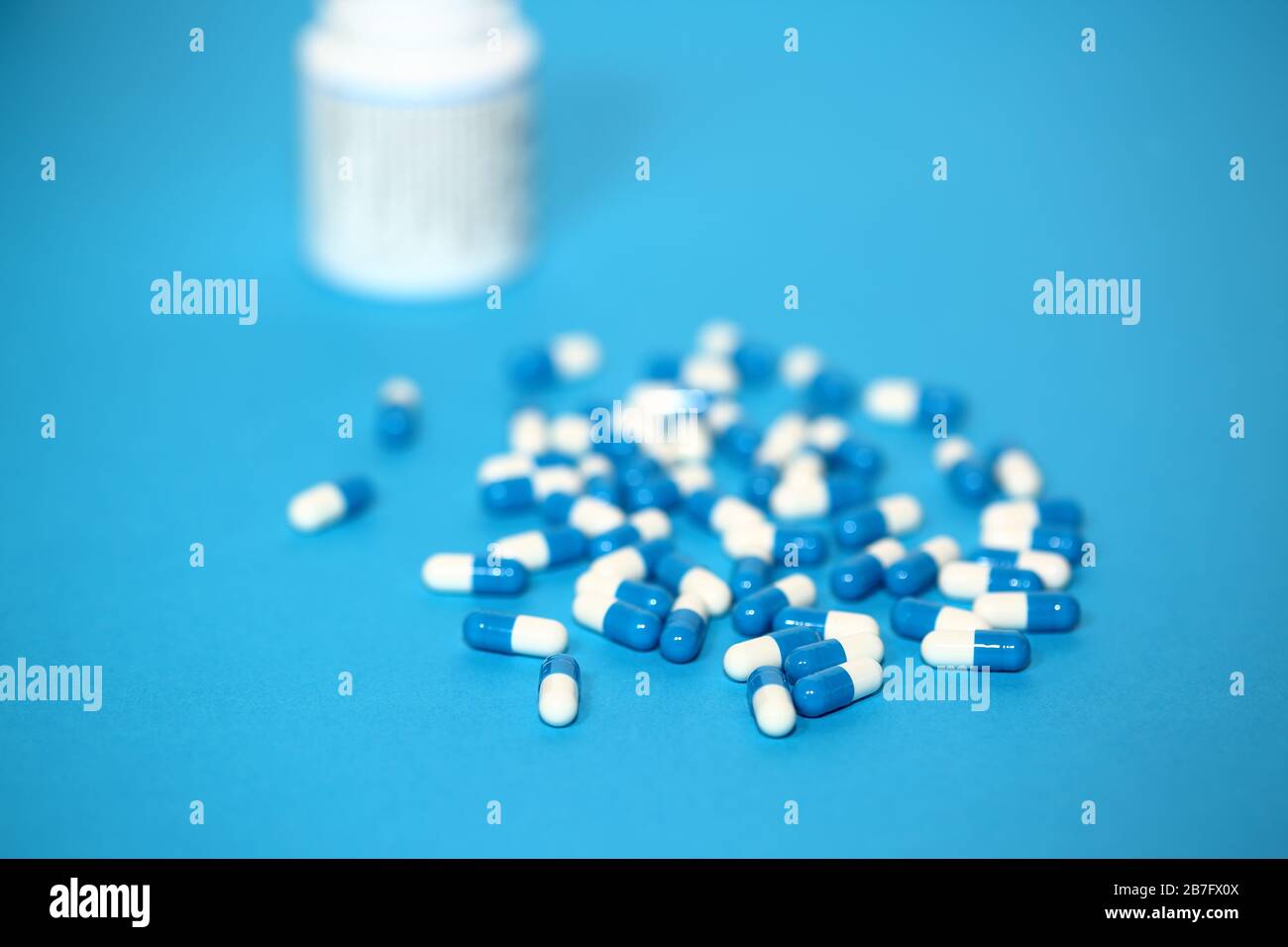 Compresse di capsuls blu e bianco a due colori isolate su sfondo blu, dietro flacone farmaceutico bianco in fuoco morbido Foto Stock