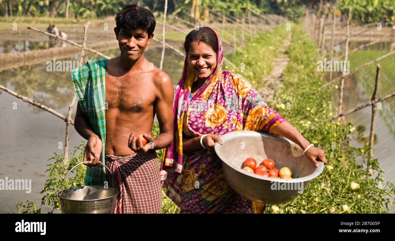 Una coppia del Bangladesh sta levandosi in piedi su una diga dello stagno con il sorriso sul face.in lo stagno producono i pesci e sulla diga producono le verdure di varietà. Foto Stock