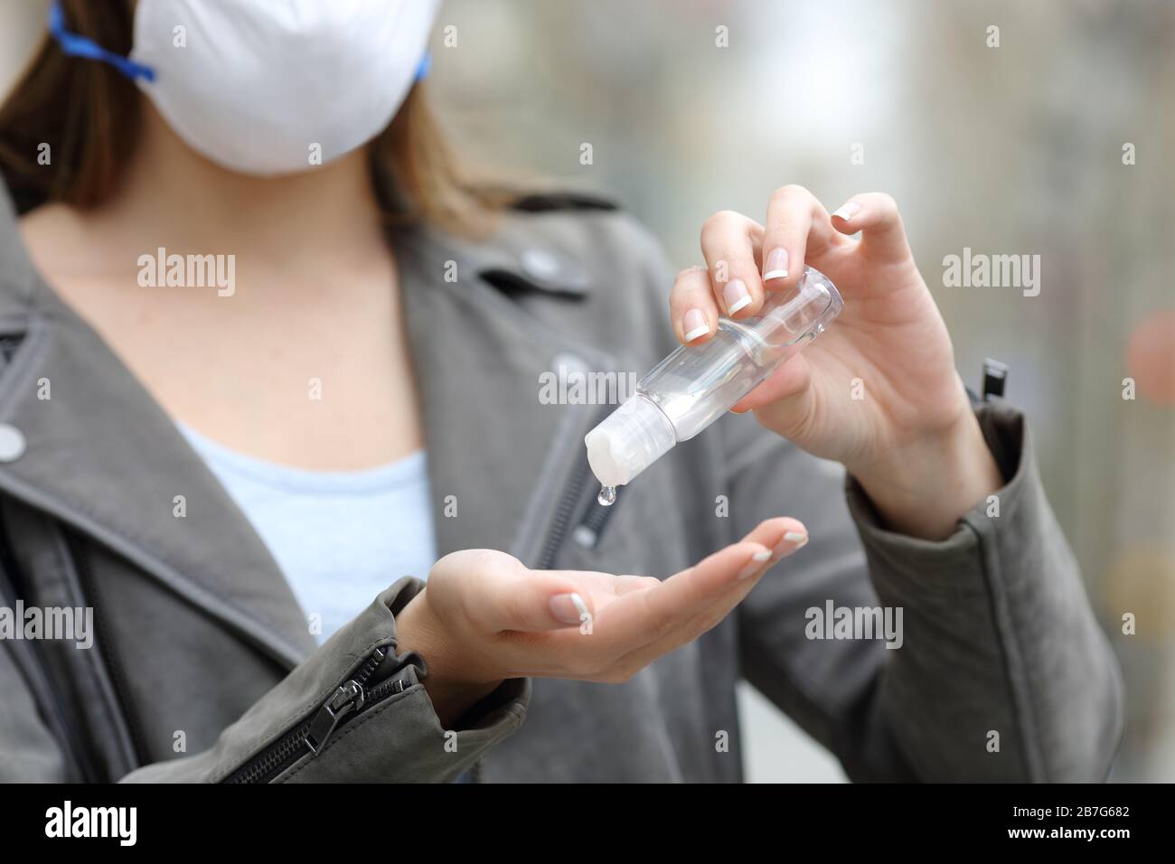 Primo piano di una donna con maschera protettiva mani igienizzanti per prevenire il contagio sulla strada Foto Stock