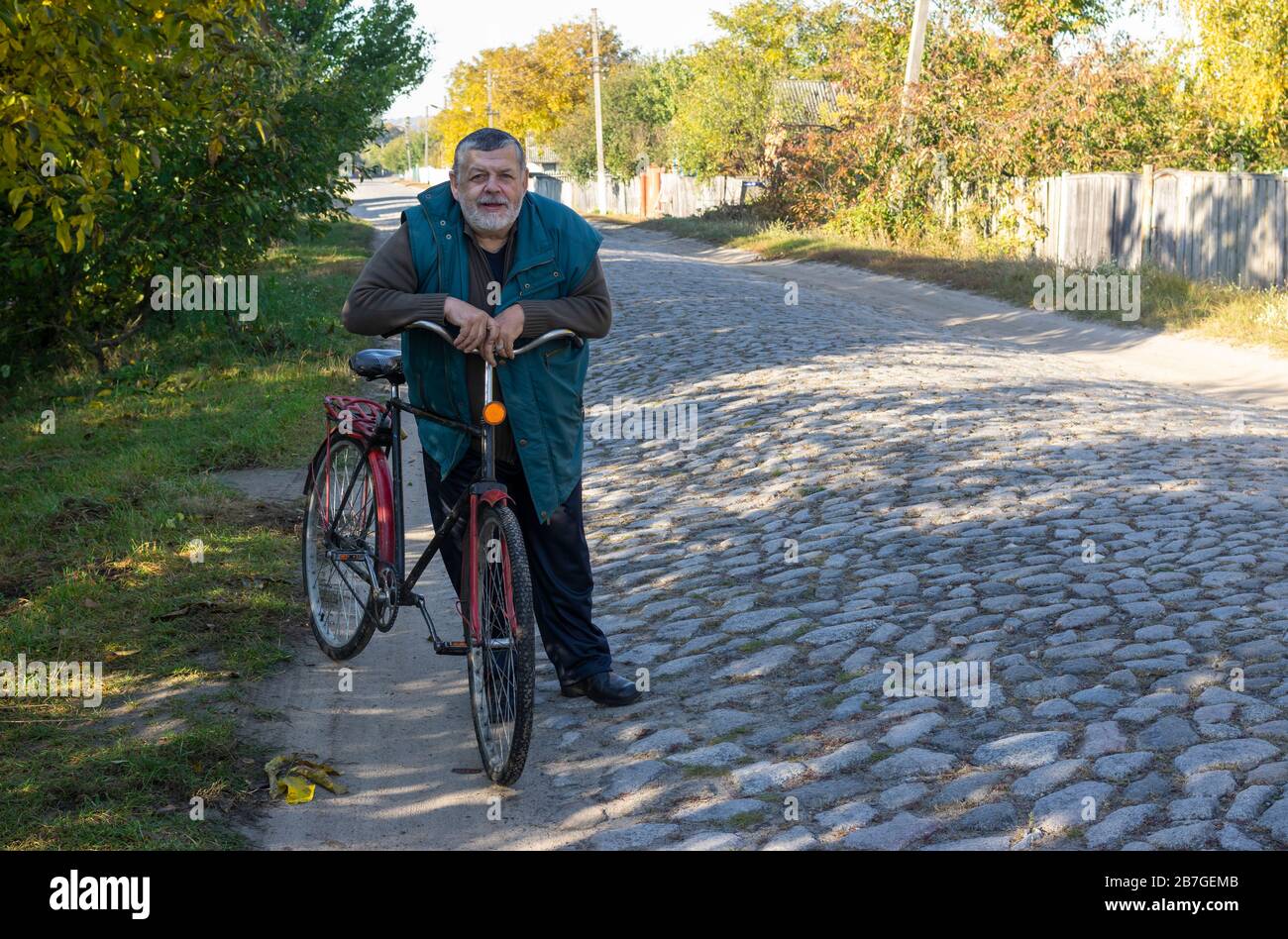 Ritratto di contadino ucraino seanior in piedi con antica bicicletta su una strada acciottolata ancien Foto Stock