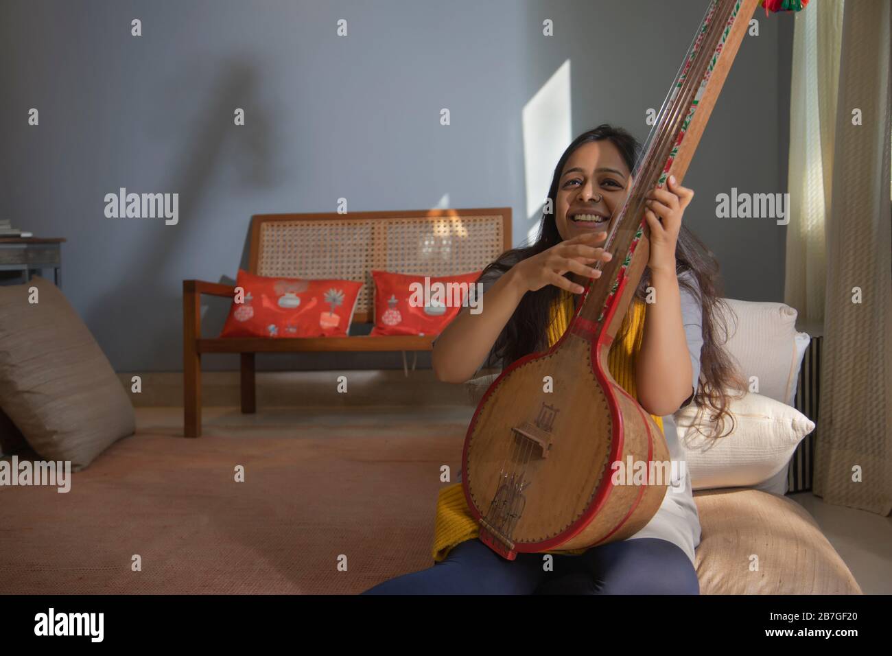 Donna che suona musica sulla sua tambura nel suo soggiorno e sorridente. Foto Stock