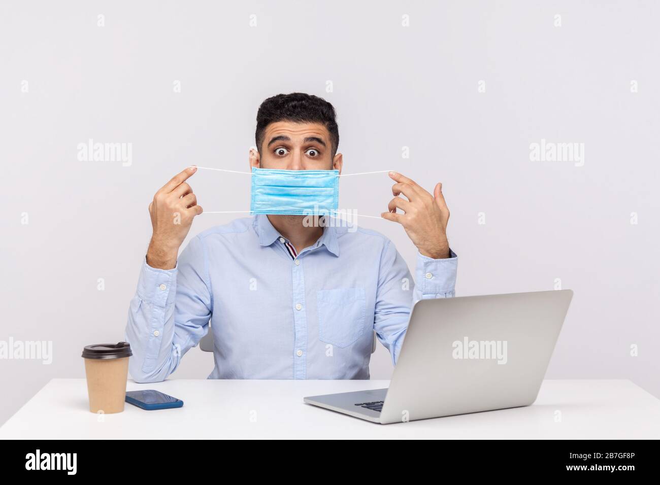 Protezione contro le malattie contagiose coronavirus sul posto di lavoro. Uomo d'affari che guarda con grandi occhi stupiti e indossando una maschera igienica seduta dentro Foto Stock