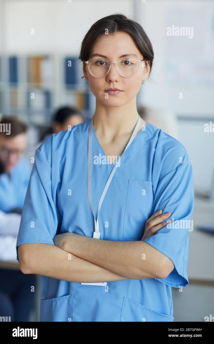Girovita ritratto di giovane infermiera che indossa occhiali in piedi con le braccia incrociate e guardando la macchina fotografica contro lo sfondo della conferenza medica Foto Stock
