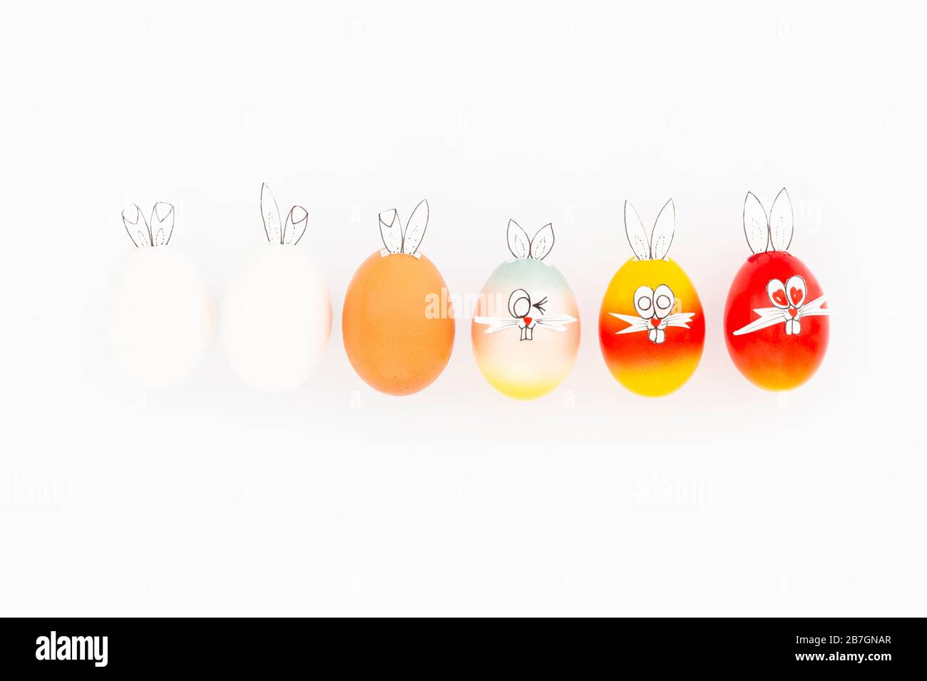 Uova di pasqua bianche, marroni e colorate dipinte con divertenti orecchie di coniglietto e facce di cartoni animati su sfondo bianco Foto Stock
