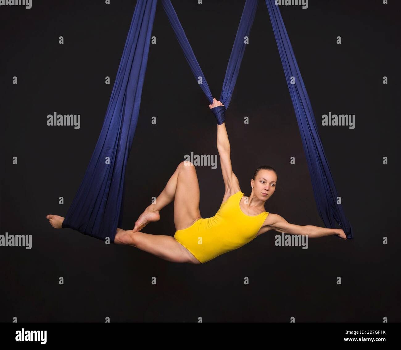 Donna giovane e sorridente che fa esercizi sulla seta aerea. Riprese in studio su sfondo scuro. Foto Stock