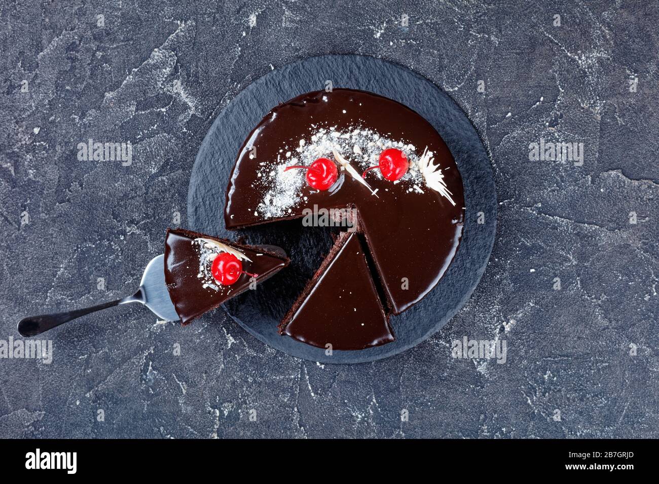 Torta al cioccolato nella foresta nera con ripieno di ciliegie con smalto al cioccolato fondente decorato con ciliegie in scatola e cioccolato bianco, una fetta posizionata Foto Stock