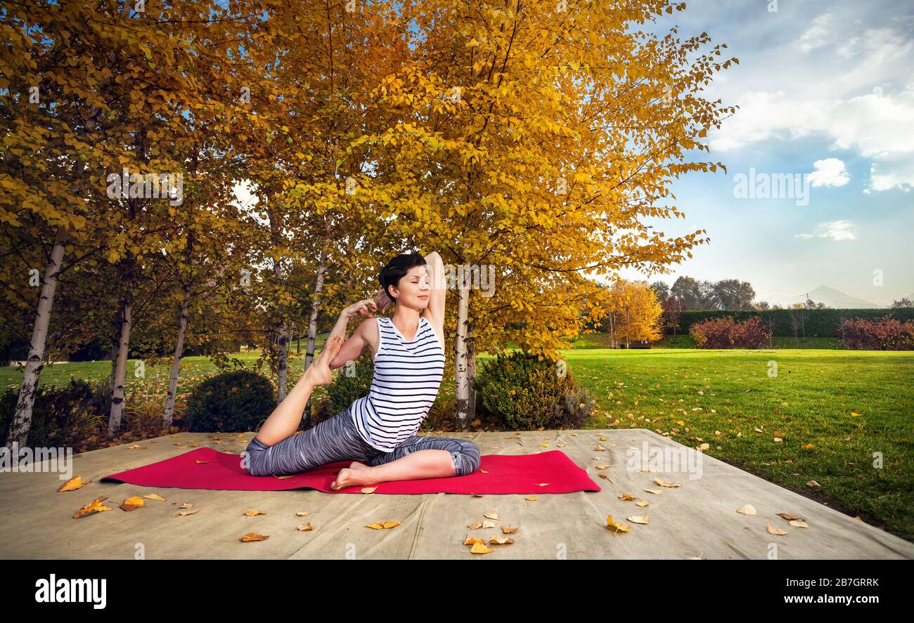 Giovane donna fare yoga in autunno il parco della città nei pressi di giallo di betulle Foto Stock