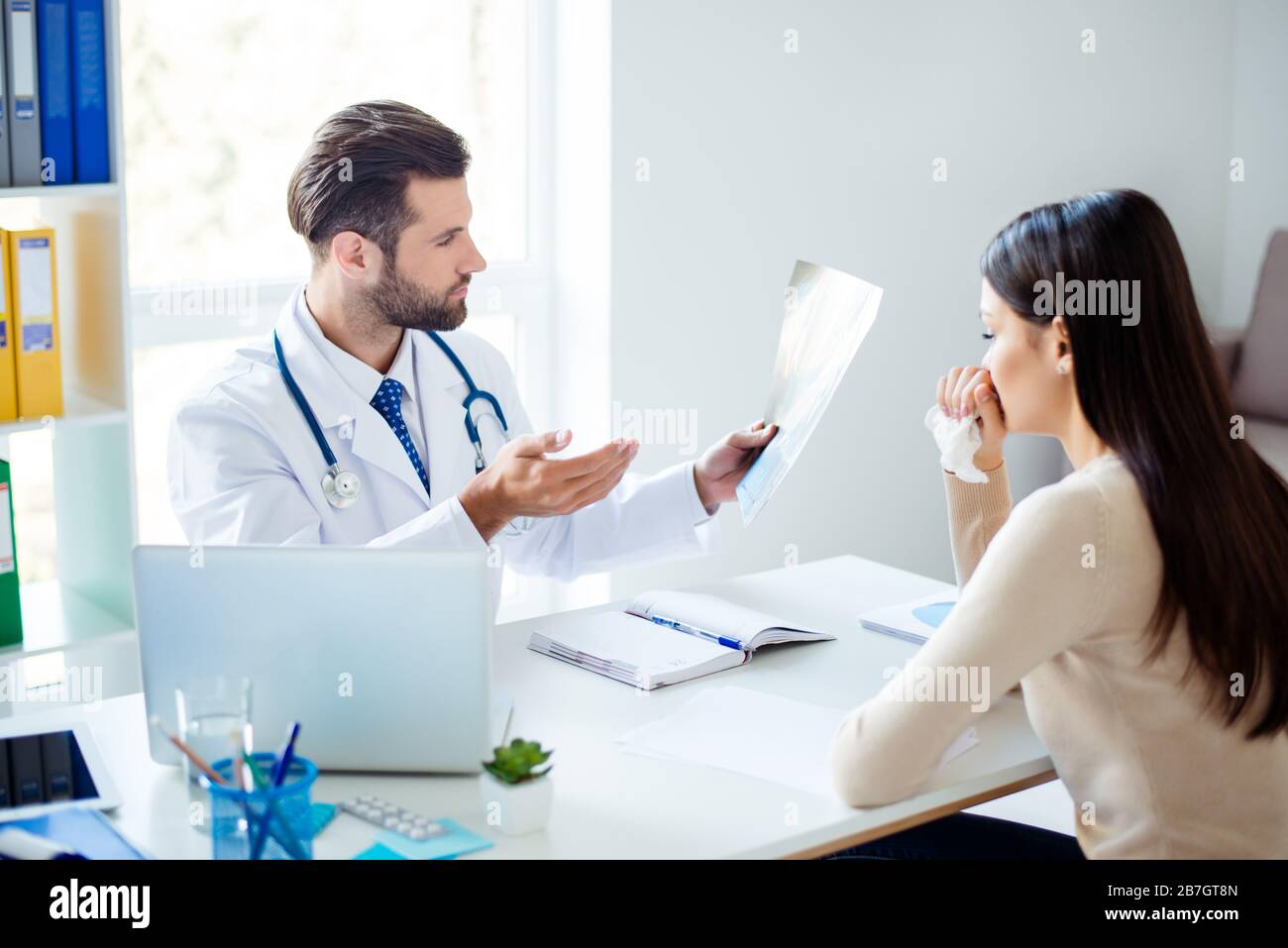 Foto di un medico che tiene i risultati della diagnosi e lo informa a turbare il paziente con un tovagliolo in mano Foto Stock