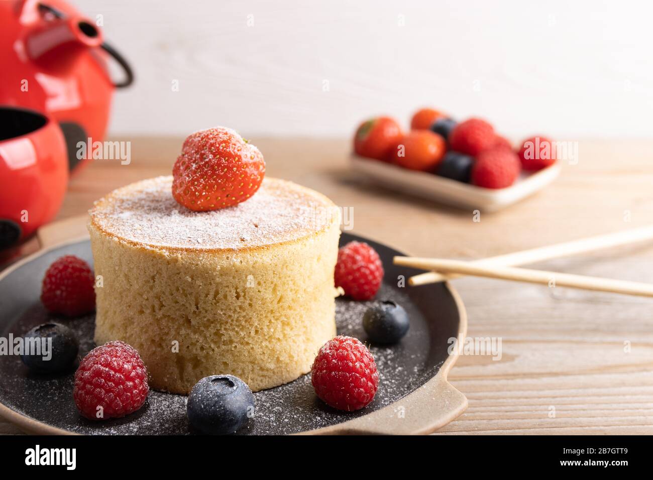 Torte giapponesi fatte in casa su uno sfondo di legno con lamponi, more e fragole e zucchero in polvere. Foto Stock