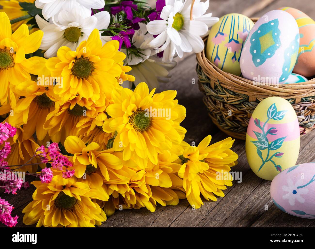 Bouquet di belle margherite gialle e colorate uova di pasqua su una superficie in legno Foto Stock