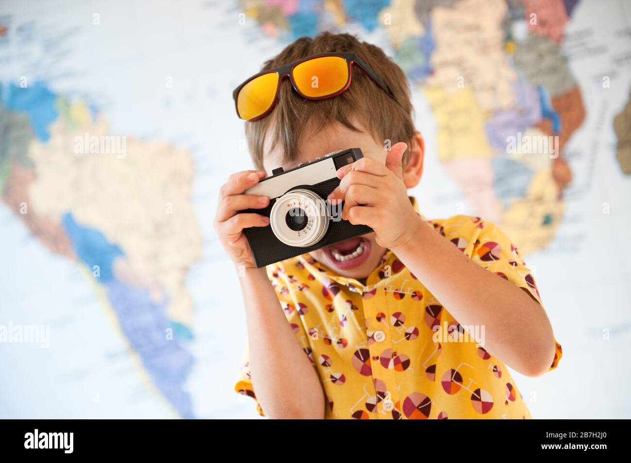 divertente ragazzino in camicia gialla estiva e occhiali da sole che scattano foto su un momento importante utilizzando la macchina fotografica del film d'epoca Foto Stock