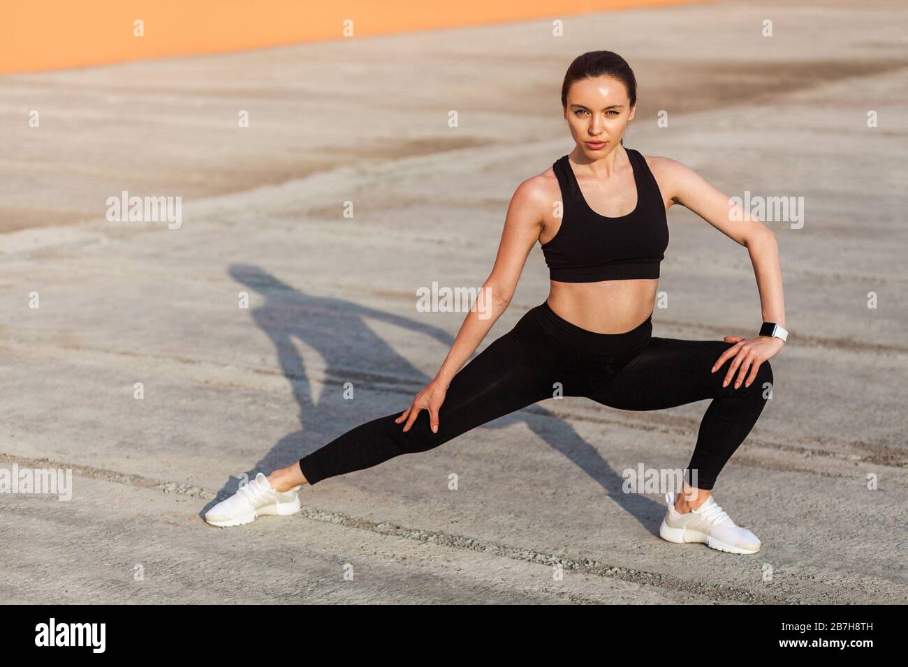 Atletica donna abbastanza in forma in stretto abbigliamento sportivo, pantaloni neri e top, pratica all'aperto, facendo stretching workout per una migliore flessibilità, basso-corpo ex Foto Stock