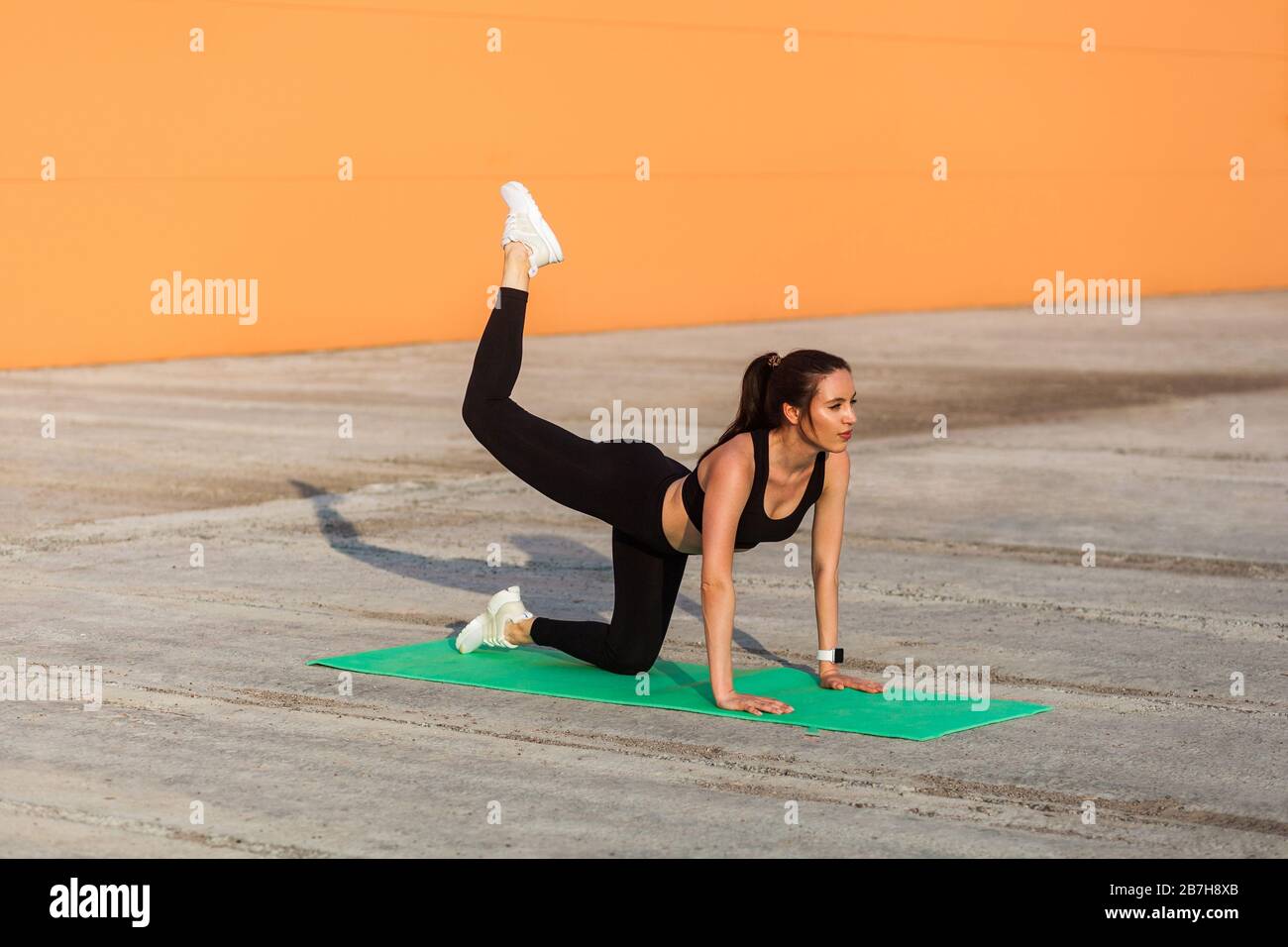 Donna bruna in forma attraente in stretto abbigliamento sportivo, pantaloni neri e top, pratica yoga, facendo una gamba con un piede posare gamba arco, allenare i muscoli e fle Foto Stock