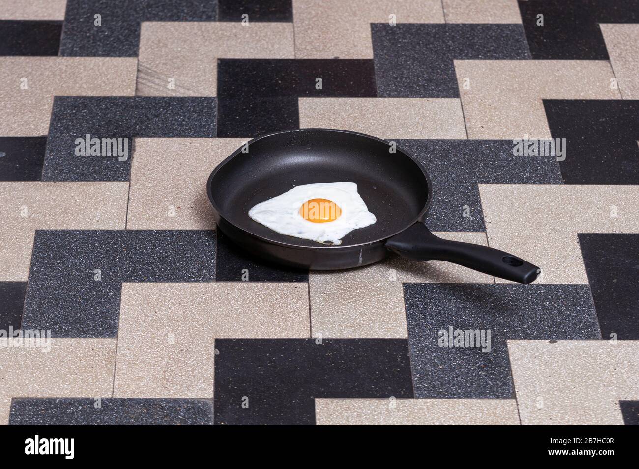 uovo cotto in una pentola nera su un pavimento di piastrelle nere e grigie Foto Stock