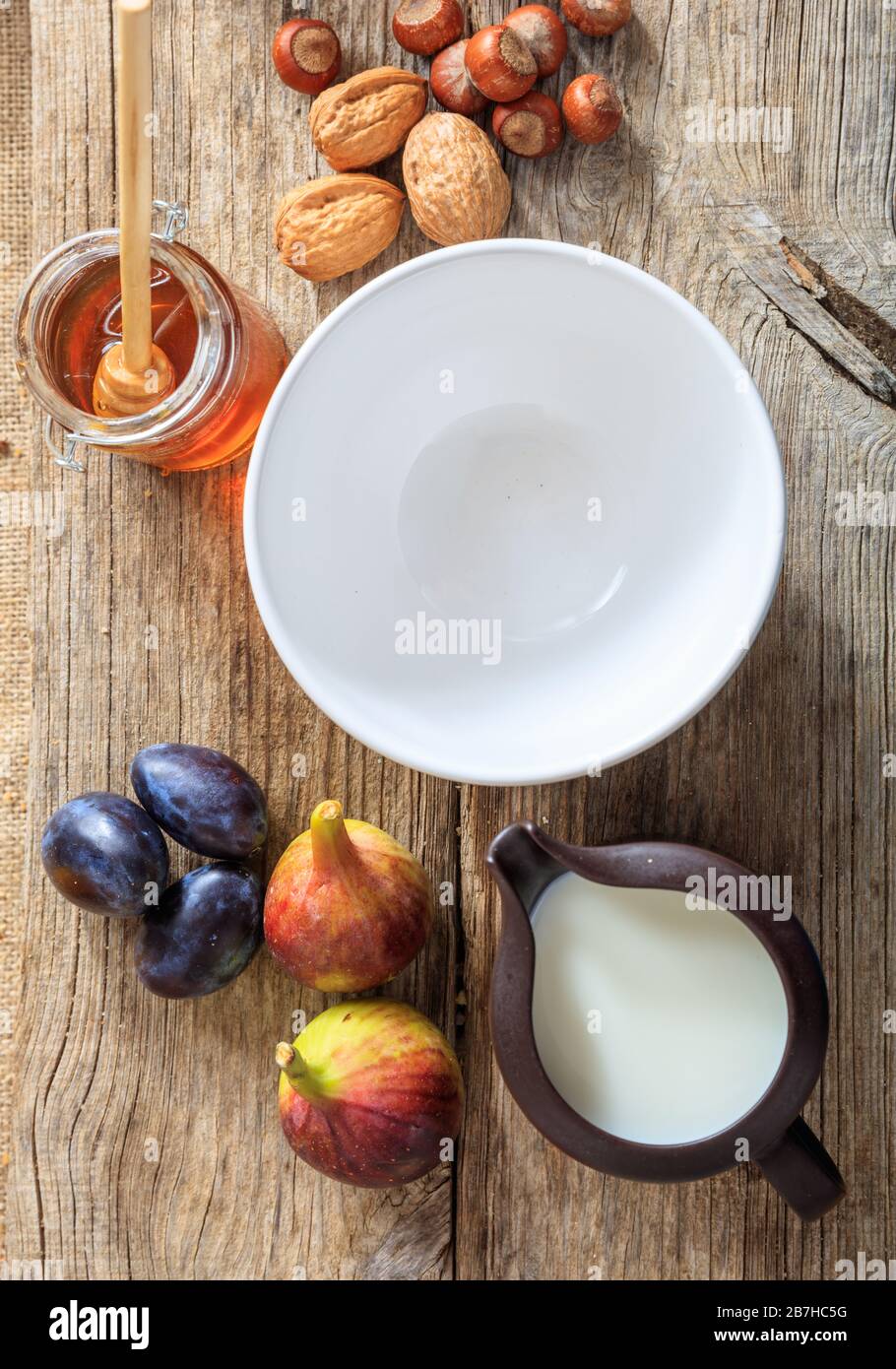 Sfondo colazione. Ciotola bianca vuota in ceramica, frutta, miele, latte e noci sul tavolo in legno. Ritratto verticale del cibo per uno stile di vita sano. Top v Foto Stock