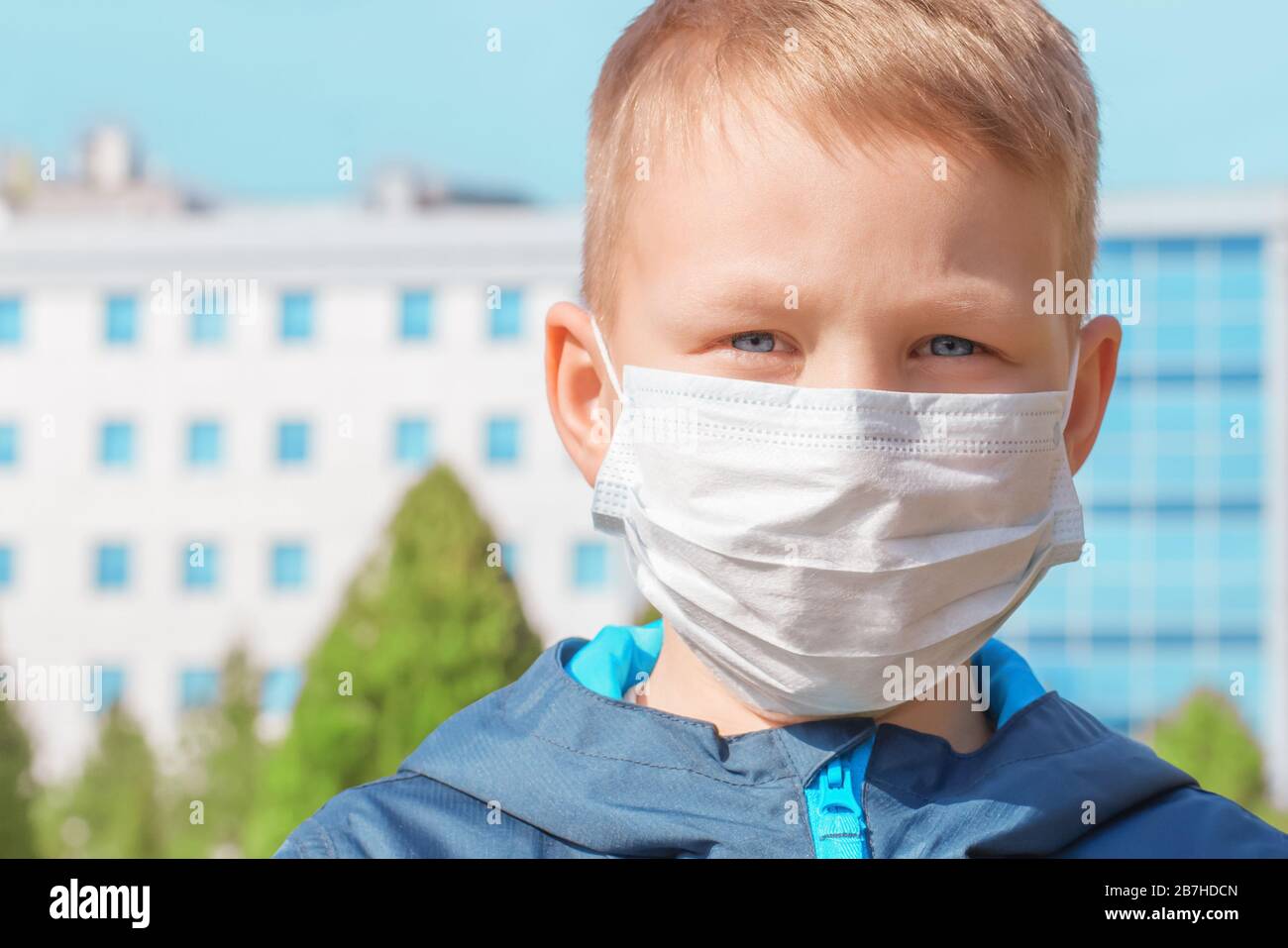 Primo piano viso di un giovane europeo in una maschera medica protettiva all'aperto sullo sfondo dell'ospedale. Protezione dai virus, prevenzione Foto Stock
