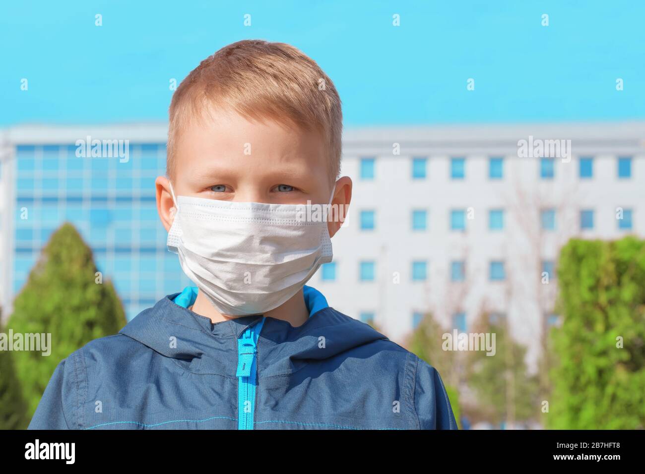 Triste ragazzo europeo in una maschera medica protettiva all'aperto sullo sfondo dell'ospedale. Prevenzione delle infezioni virali, concetto di protezione dai virus Foto Stock